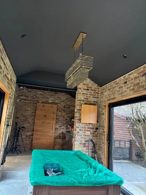 Brick built garden room with a vaulted dark ceiling, bifold doors and brass pendant lights hung over a pool table